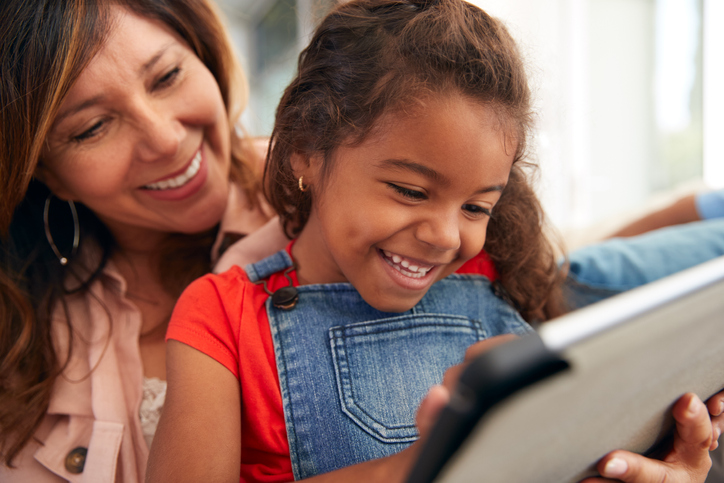 Granddaughter With Grandmother Sitting On Sofa At Home Using Digital Tablet